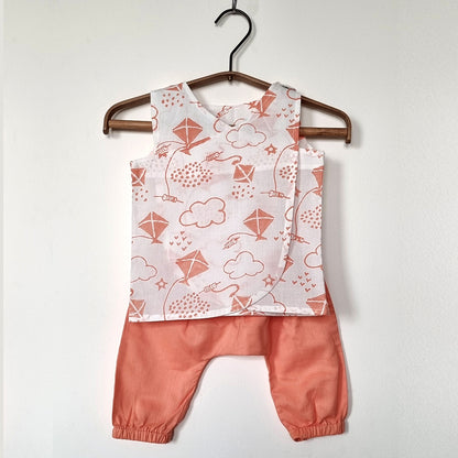 Baby outfit with a patterned top and pink pants on a hanger against a white background