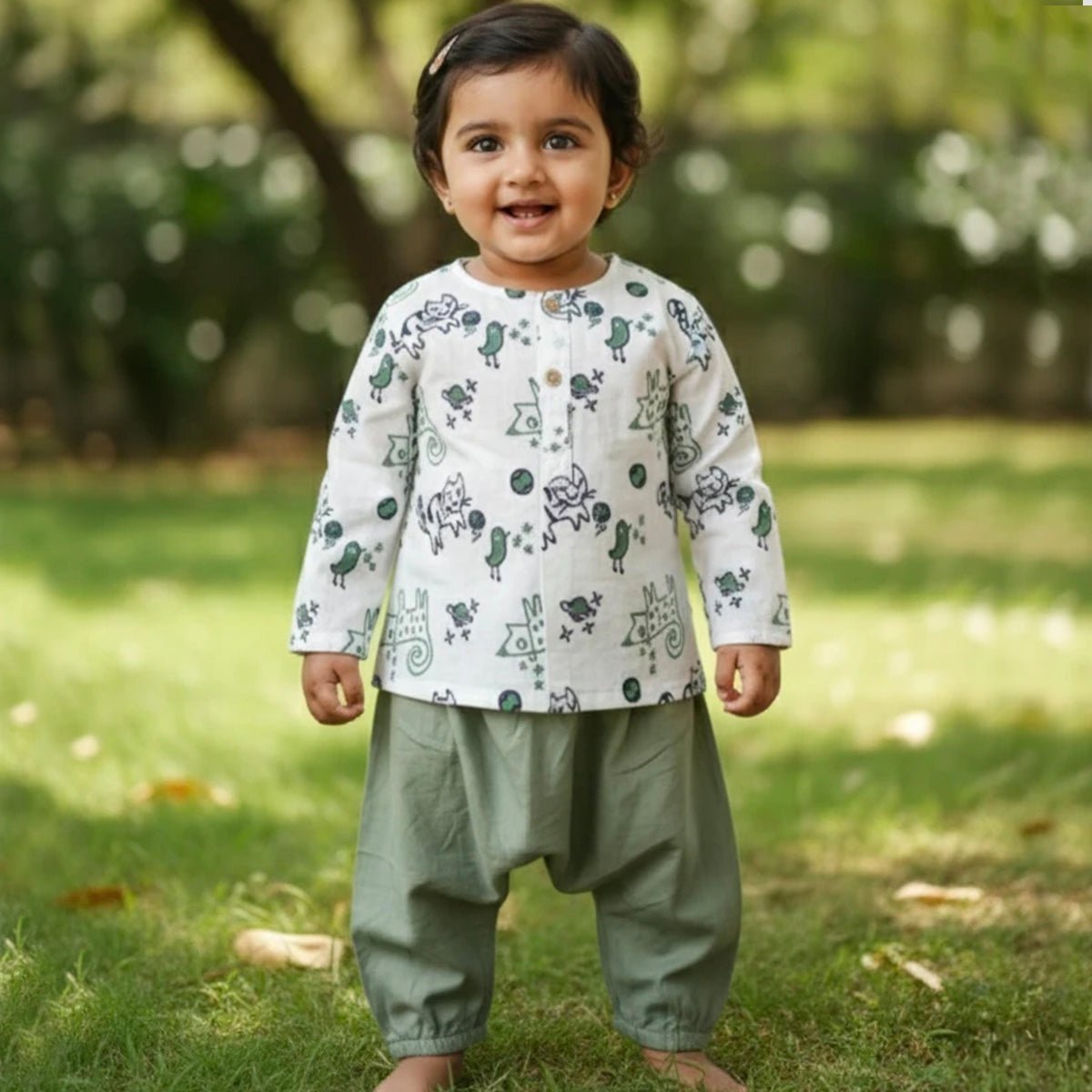 Child wearing a patterned shirt and green pants standing on grass with a blurred natural background